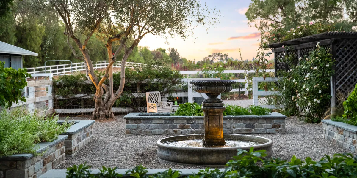 Elegant backyard landscaping with a rustic stone fountain, lush greenery, and a peaceful garden setting at sunset, creating a serene outdoor retreat.