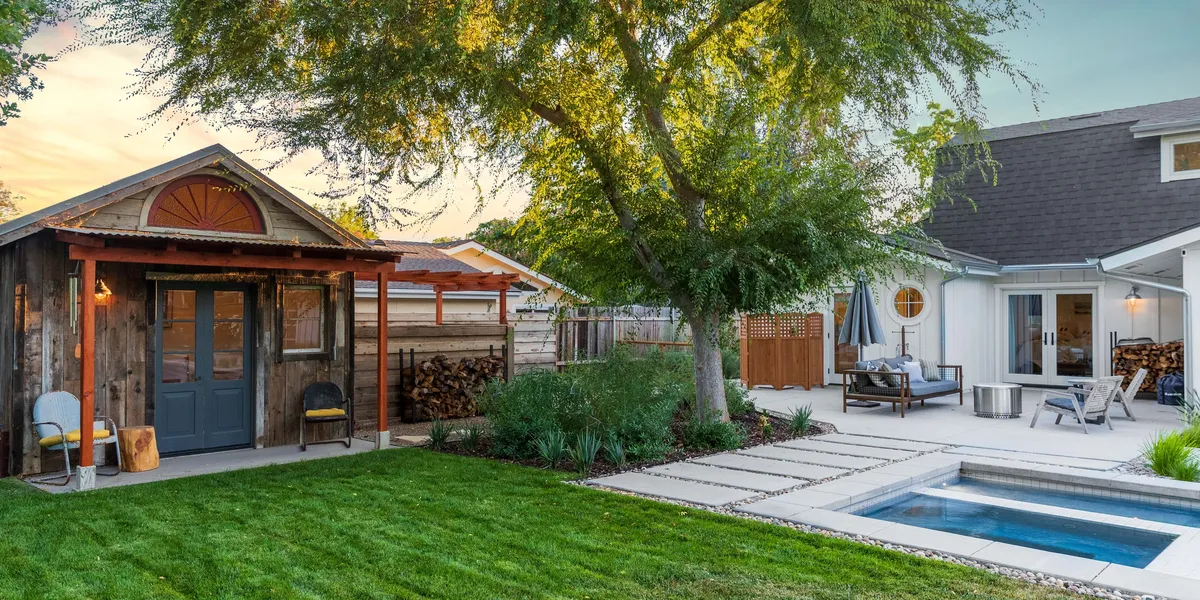 Beautifully landscaped backyard featuring a lush green lawn, rustic wooden shed, modern patio seating area, and a small pool, creating a cozy outdoor retreat serviced by AAA Landscaping.