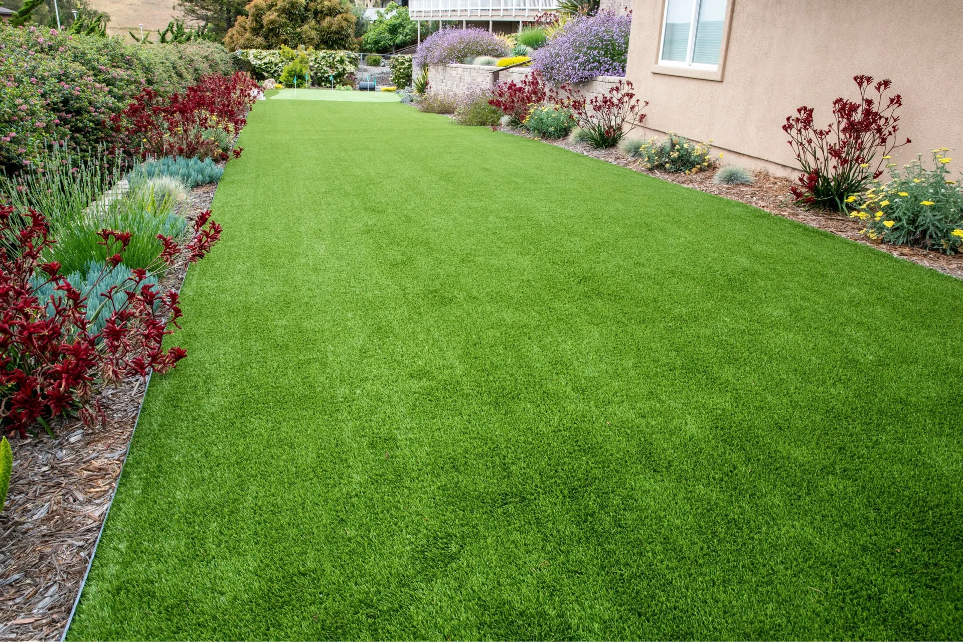 Lush green synthetic turf in a beautifully landscaped backyard, offering a low-maintenance, eco-friendly lawn solution for a perfect outdoor space.